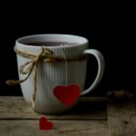 A cup of tea with a heart-shaped tag and another heart fallen on a wooden table, symbolizing love, heartbreak, and personal transformation.