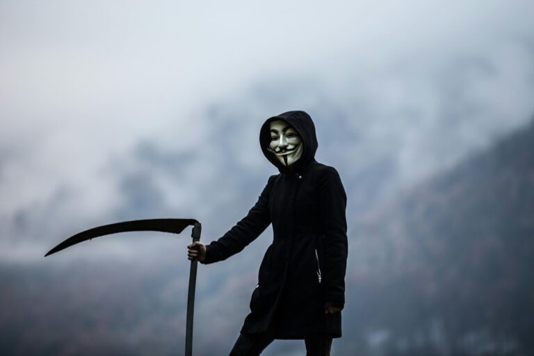 A hooded figure in a Guy Fawkes mask holding a scythe, symbolizing layoffs, career uncertainty, and transformation.